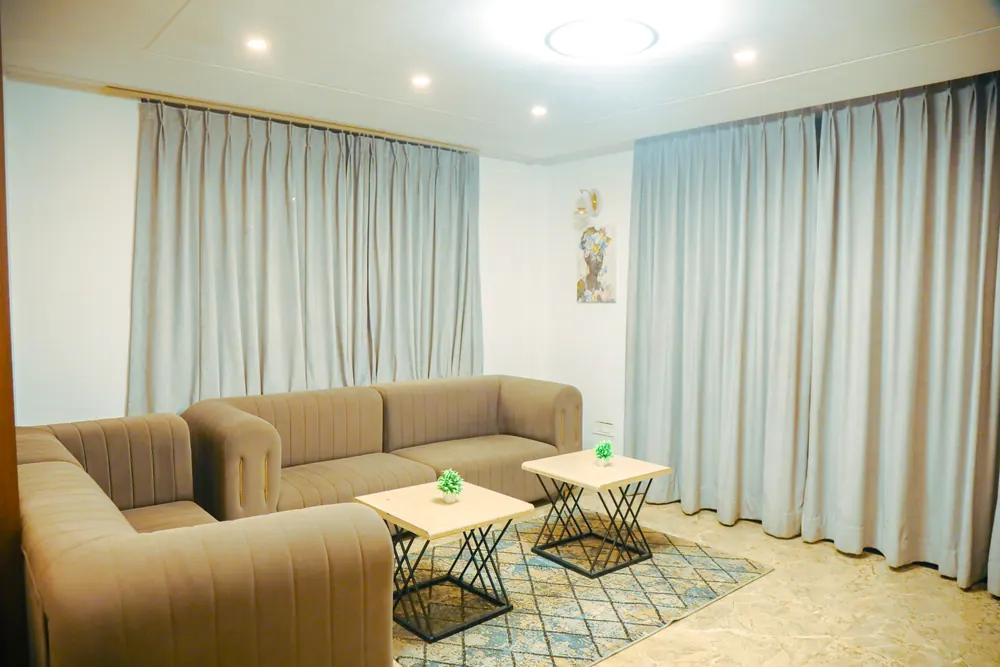 Corner sofa with two small side tables on a patterned rug in front of pale curtains