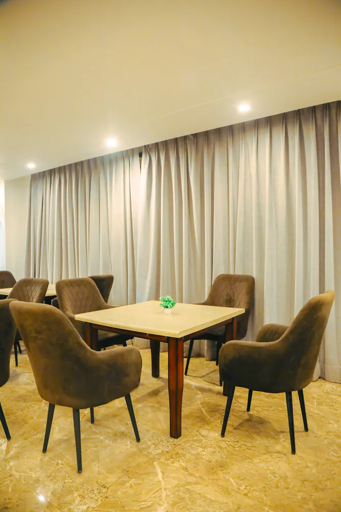Wooden table with four upholstered chairs in front of floor-length curtains
