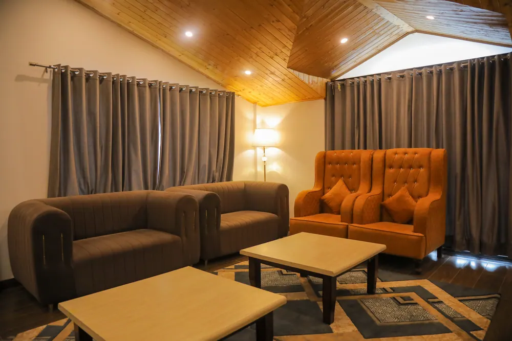 Lounge with grey sofas, orange tufted armchairs, wooden coffee tables and curtained windows under a timber ceiling
