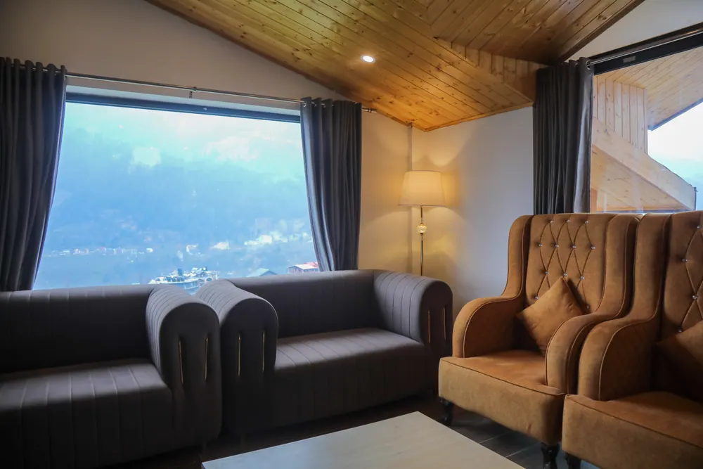Grey sofas and an orange armchair facing a large window with a view over the valley