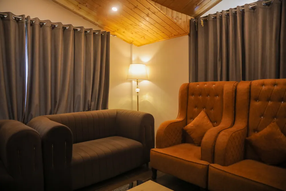 Close view of orange tufted armchairs and a grey sofa beside heavy curtains and a floor lamp