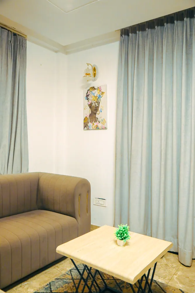 Taupe sofa and a small wooden side table with a plant beside floor-length curtains