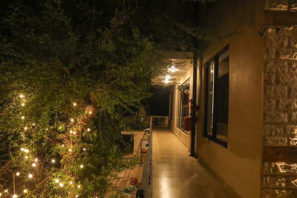 Lit terrace walkway at night beside a stone-clad wall, with fairy lights glowing in the greenery
