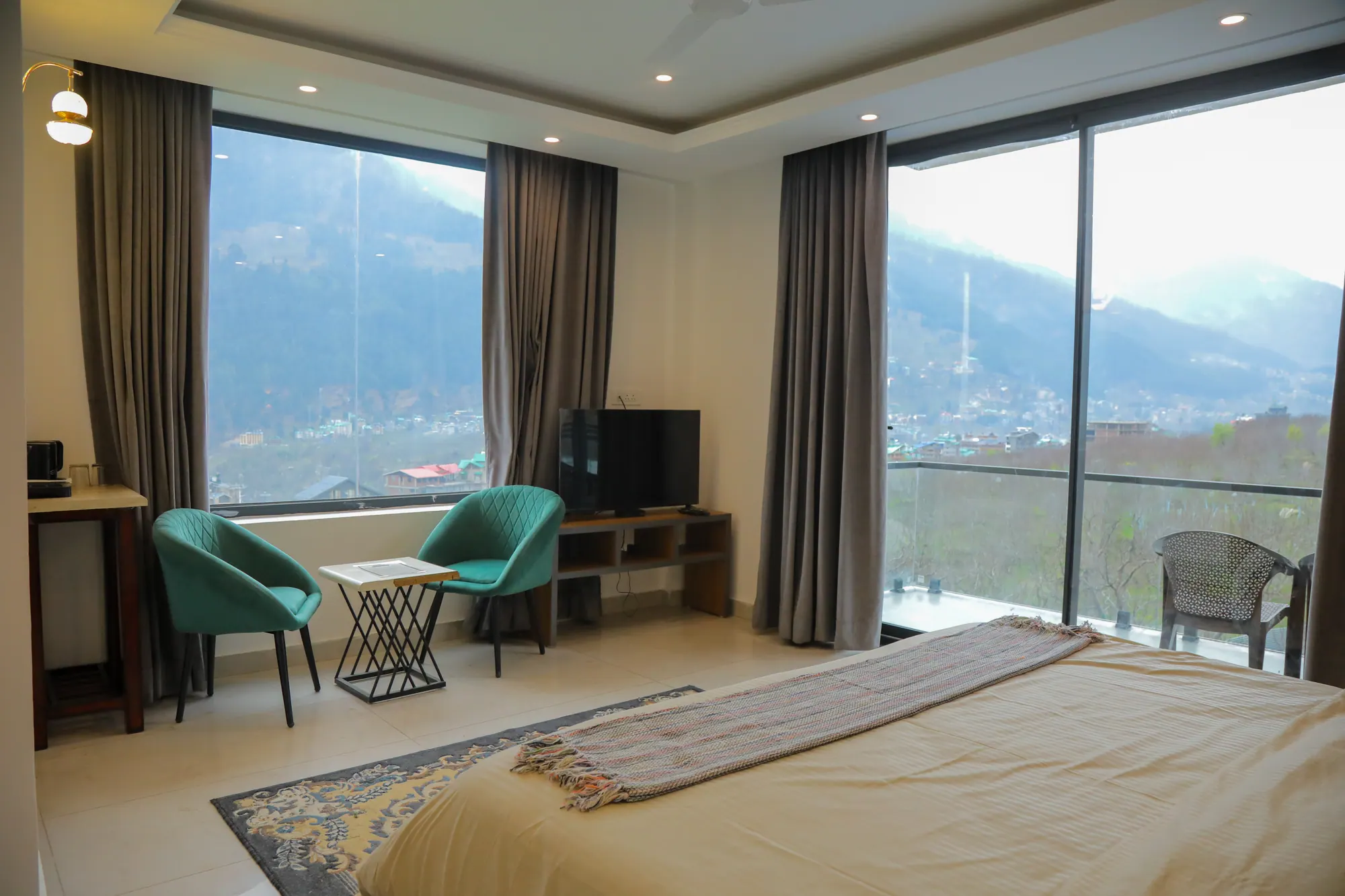 Bedroom with large windows and a balcony door looking out over the Manali valley and mountains