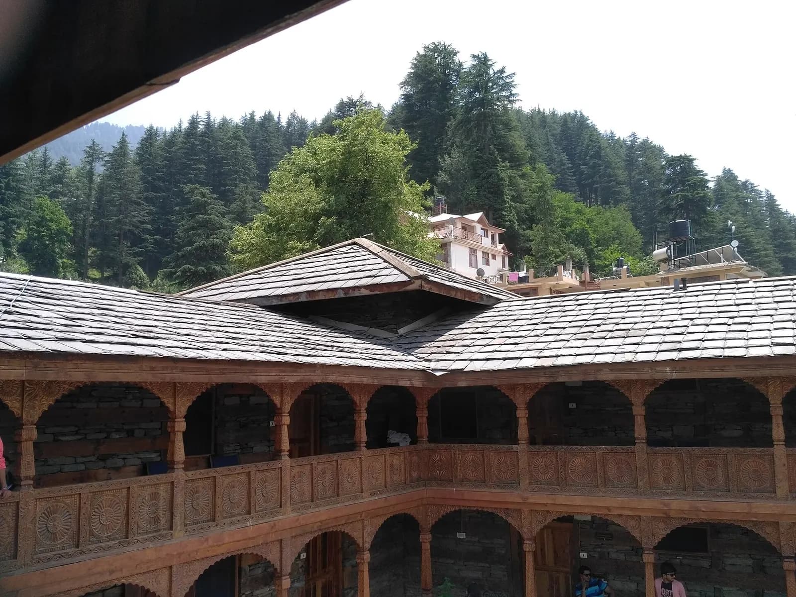 Carved wooden balconies and slate roofs around the courtyard of Naggar Castle, with deodar forest rising behind