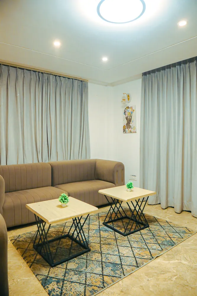 Lounge with a taupe sofa, two side tables and a patterned rug beneath a round ceiling light