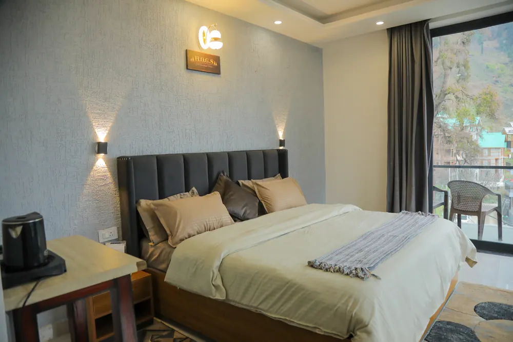 Bedroom with a grey headboard wall, a glass door to a balcony with a chair and an electric kettle on a side table
