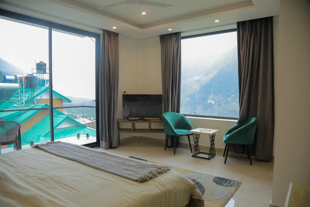 Bedroom with corner windows, a balcony door, a television unit and two green armchairs